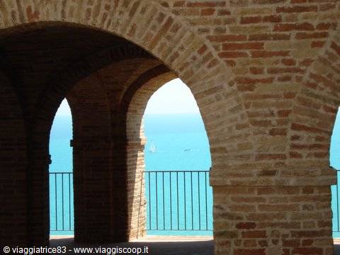Brick arches frame the turquoise sea with a sailboat in the distance