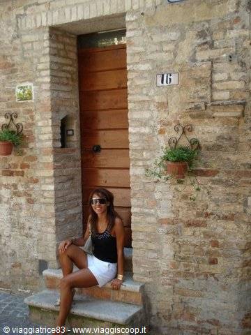 Woman with sunglasses sitting on stone steps before wooden door, brick wall