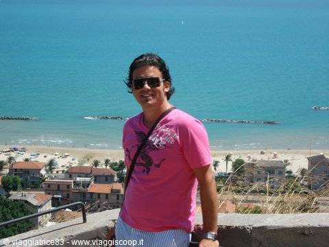 Man in pink t-shirt and sunglasses on terrace overlooking beach and turquoise sea