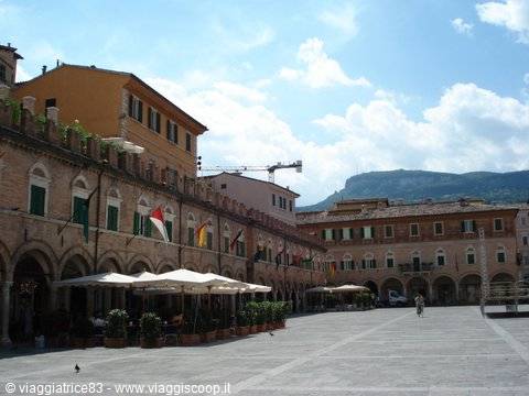 Piazza del Popolo in Ascoli Piceno: travertine arcades, flags and cafés under white umbrellas