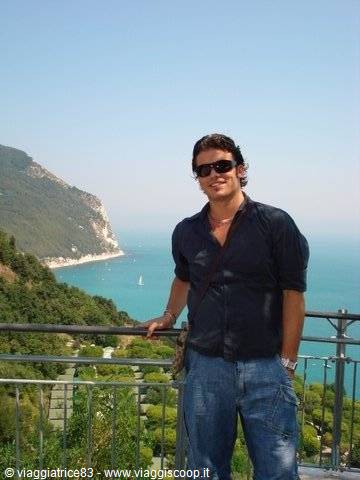 Smiling man in sunglasses by a railing, Monte Conero coastline and turquoise sea behind