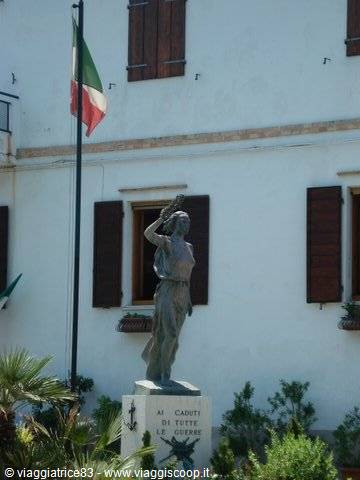 Stone statue of woman saluting in front of white building, Italian flag, war memorial