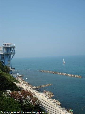 Sailboat near the rocky breakwater, stepped stairway and blue building by the sea