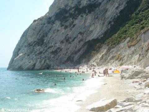 Bathers on pebbly beach beneath limestone cliff, turquoise sea