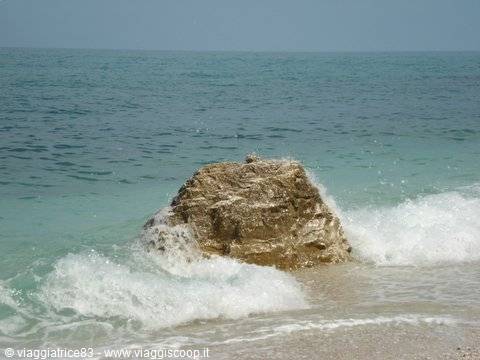 Foamy waves crash against a large rock at the beach