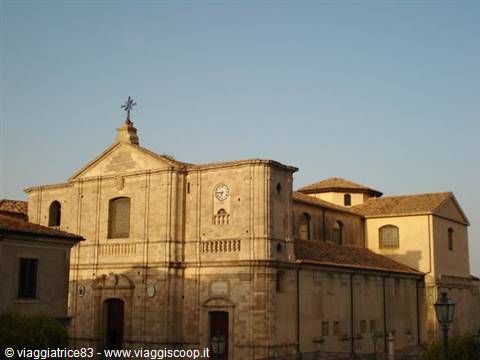 Stone church with facade, clock and cross, lit by afternoon sun