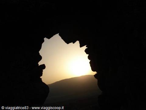 Sunlight filtering through dark cave rocks, hill silhouetted against the glow