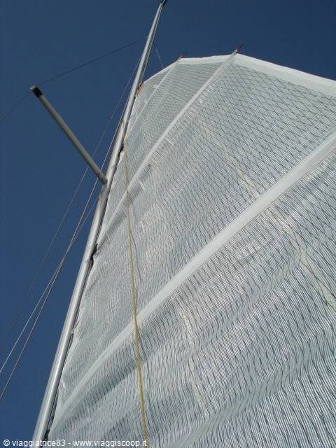 White sail billowing against blue sky, metal mast and rigging in the foreground