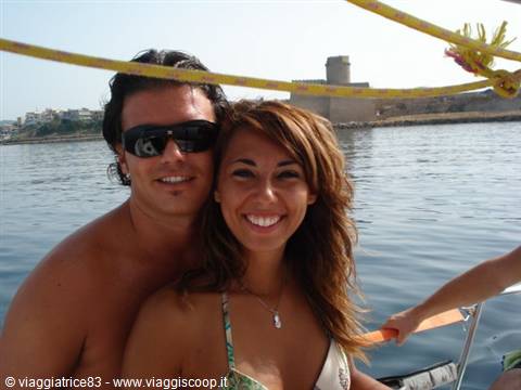 smiling couple on a sailboat, coastal tower in the background