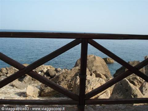 Wooden railing in front of rocks and blue sea under clear sky