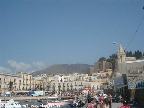 Tourists stroll among boats at Lipari harbor, beneath the castle and church