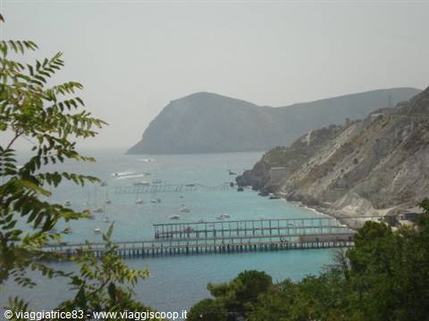 Pier over turquoise sea with boats, white cliffs and green leaves, Ischia