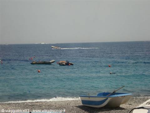 Blue rowboat beached on pebble shore, boats and swimmers in turquoise sea