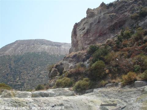 Yellow volcanic rocks with red stains among shrubs under a blue sky