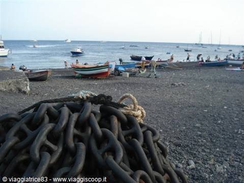 Iron chains on black pebble beach, boats and swimmers by the sea