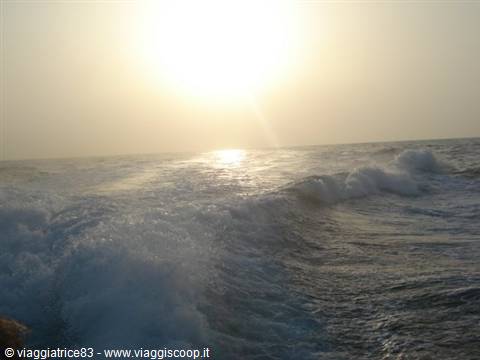 White waves crash on the sea under a low hazy sun