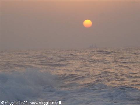 Orange low sun over hazy sea, foamy waves in the foreground