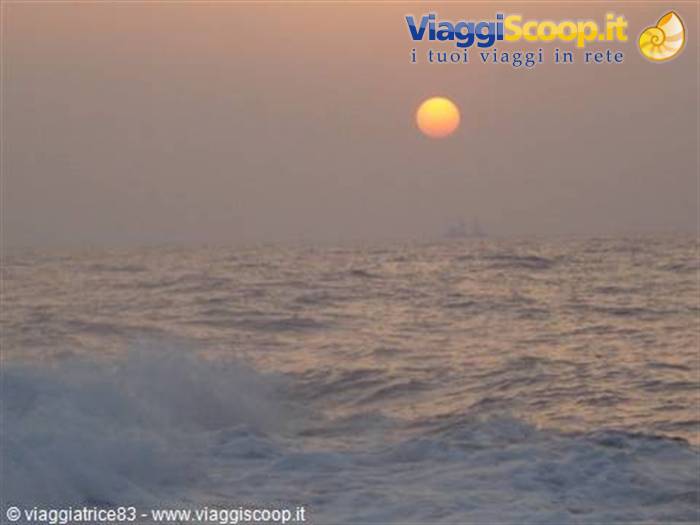 Orange low sun over hazy sea, foamy waves in the foreground