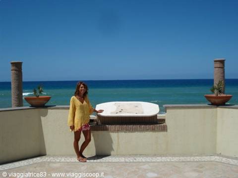 Woman in yellow tunic beside a tub on a terrace overlooking the sea