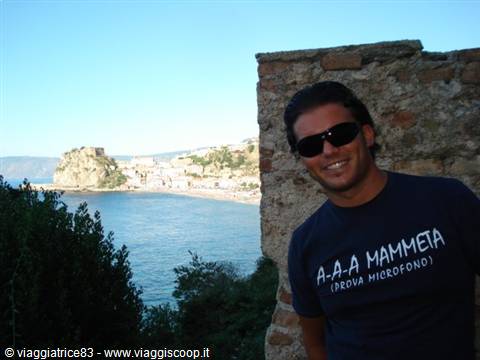 Sunglasses tourist beside an old stone wall, Aragonese castle of Scilla behind