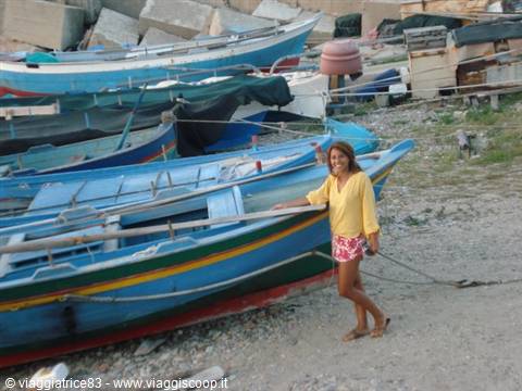 Woman in yellow shirt beside blue wooden fishing boats on pebble beach