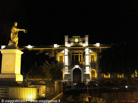 Marble statue lit beside a historic building glowing at night