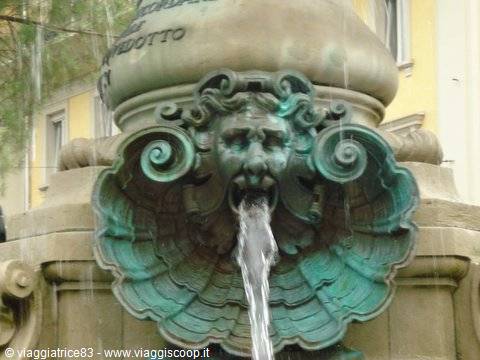 Weathered green bronze mask spouting water into a stone shell fountain