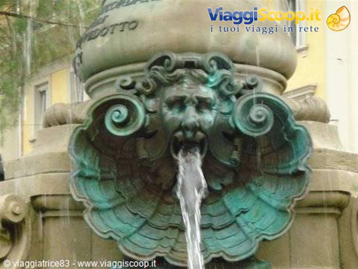 Weathered green bronze mask spouting water into a stone shell fountain