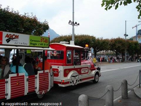 Red tourist road train carrying passengers along Lugano lakeside promenade