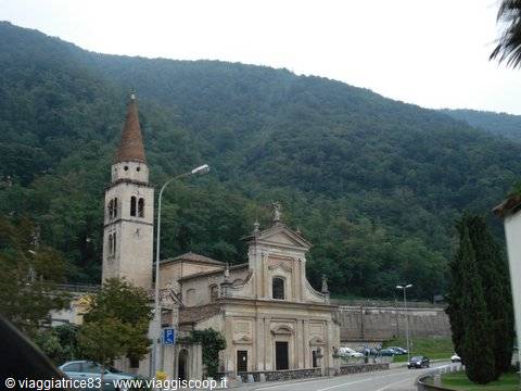 Stone church with bell tower, parked cars, green rain-soaked hills behind