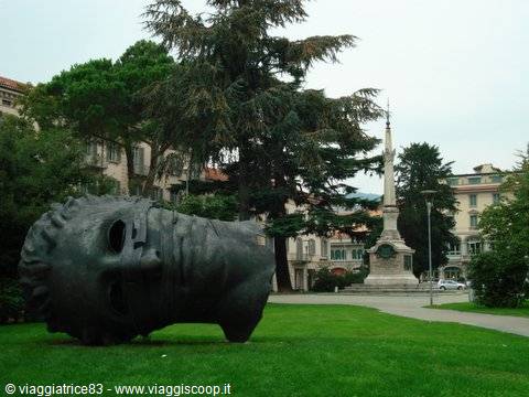 Huge bronze head by Mitoraj on the lawn, an obelisk behind the trees