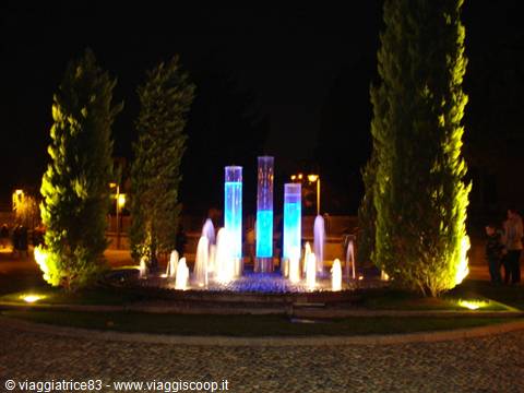 Illuminated fountain at night with water jets and blue cylinders among cypresses