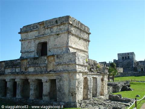 Mayan stone ruins at Tulum under blue sky, green lawns nearby