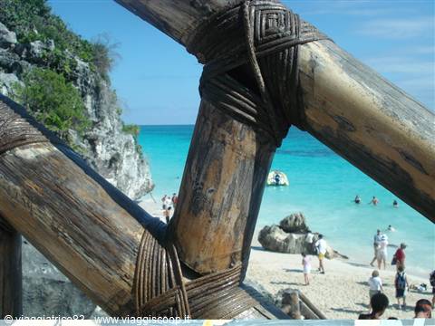 Wooden railing tied with rope overlooking a beach, cliffs and turquoise sea