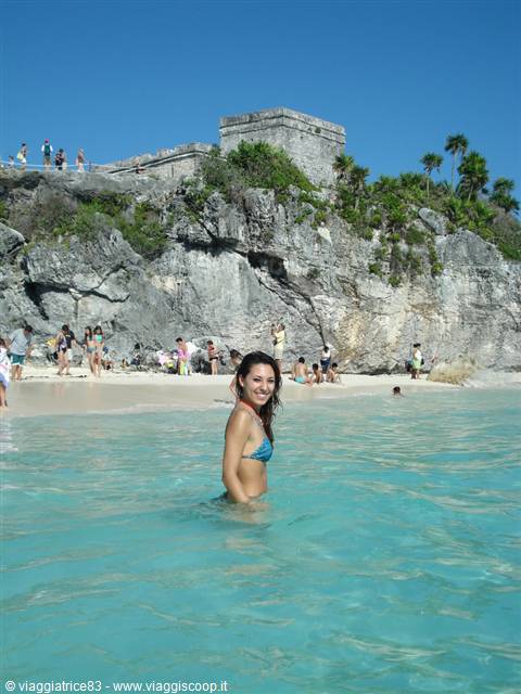 Tourist in turquoise water beneath the Mayan ruins of Tulum