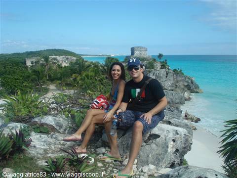 Tourists sitting on rocks in front of Tulum Mayan ruins and turquoise sea