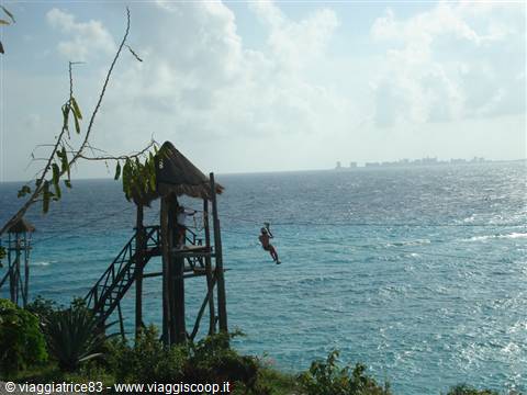 Zipline rider over turquoise sea, wooden tower with thatched roof