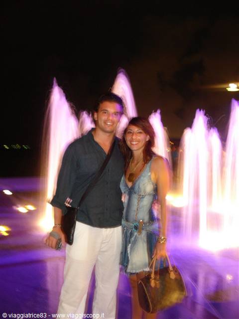 Smiling couple in front of the purple-lit fountain at night