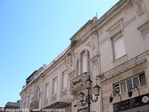 Light stone facade with balcony, wrought-iron street lamps and blue sky