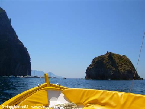 Yellow boat bow near rocky sea stacks and blue water under clear sky