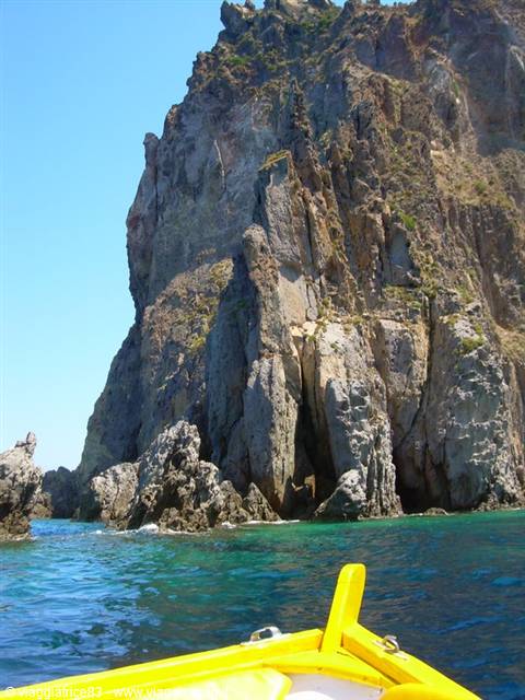 Yellow boat bow facing volcanic cliffs over turquoise sea, Aeolian Islands