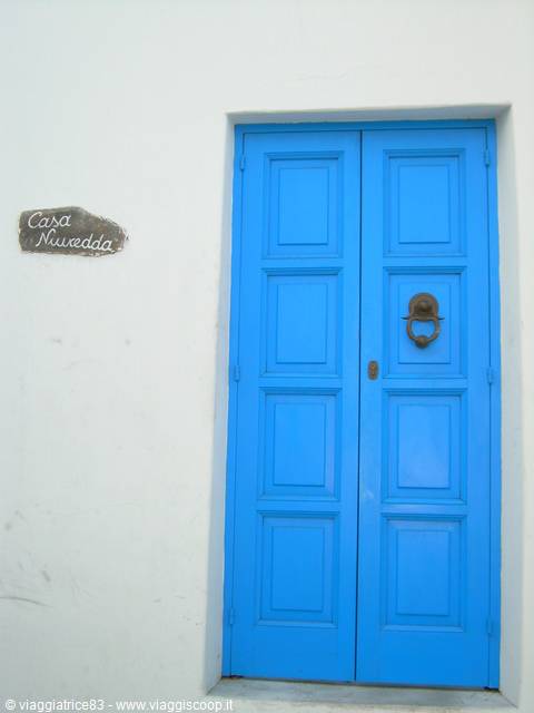 Blue double wooden door with iron knocker on white lime-washed wall