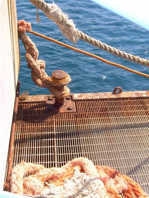 Worn ropes tied to a rusty bollard on the ship's metal deck