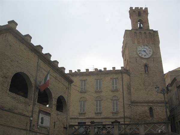 Brick clock tower with crenellations, town hall building, Italian flag, gray sky