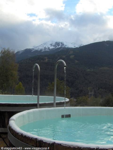 Wooden hot tubs with turquoise water, metal spouts pouring water, snowy mountains behind