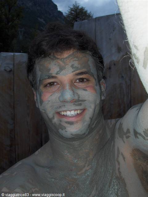 Smiling man with his face covered in mud, inside an outdoor wooden tub