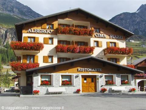 Albergo Cima Piazzi wooden and stone hotel, red geranium balconies, mountains behind