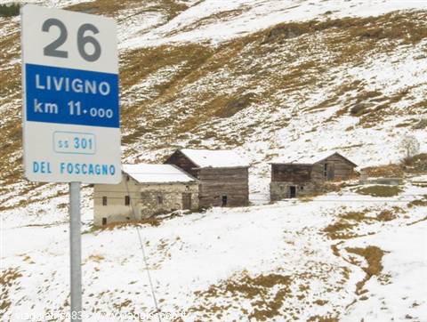 Road sign to Livigno by snow-covered wooden and stone mountain huts