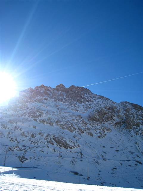 Bright sun over a snow-covered rocky mountain slope, ski run below