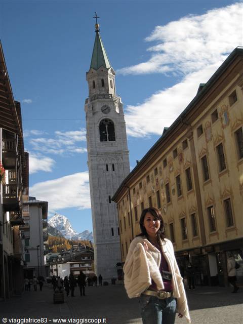 Smiling woman in front of Cortina d'Ampezzo bell tower among painted buildings